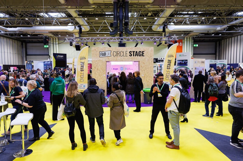 A large group of diverse individuals gathered in a convention hall, engaging in conversation and networking.