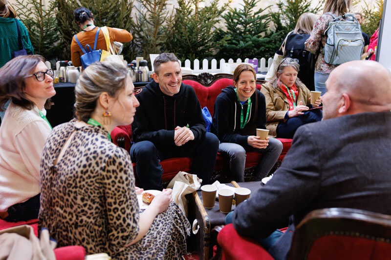 A group of people seated around a table in a room adorned with trees, engaged in discussion at the FAB UK show.