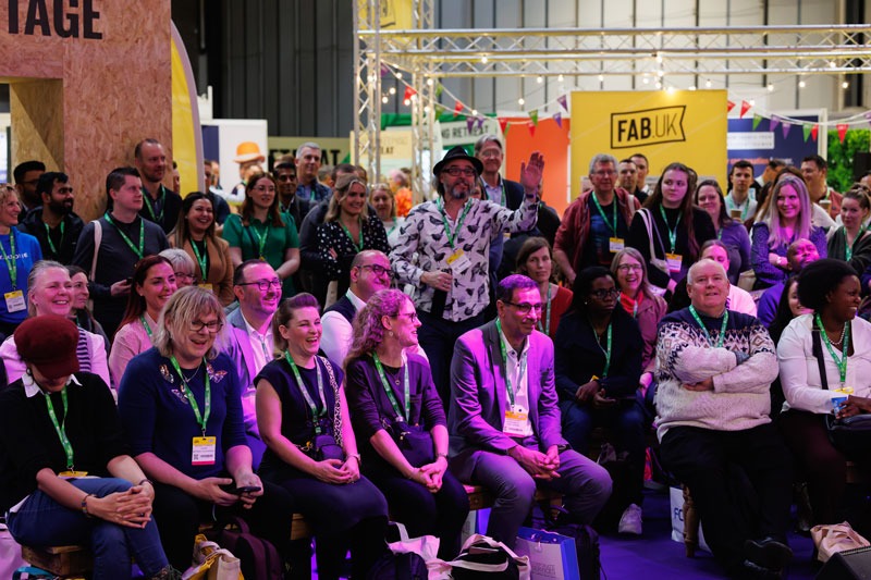 A large audience seated in front of a stage at the FAB UK show, engaged and attentive to the presentation.