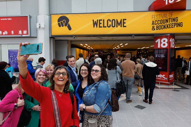 Group of people smiling at camera while taking selfie in front of FAB UK sign